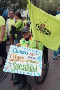 Fotografía en plano general de una mujer usuaria de silla de ruedas que sostiene un cartel que dice “Quiero ser libre para disfrutar de mi sexualidad”, durante el Tercer Recorrido por el Día Internacional de las Personas con Discapacidad.