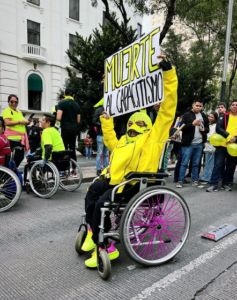 Fotografía en plano general de un hombre usuario de silla de ruedas que sostiene un cartel que dice “Muerte al capacitismo”, durante el Tercer Recorrido por el Día Internacional de las Personas con Discapacidad.