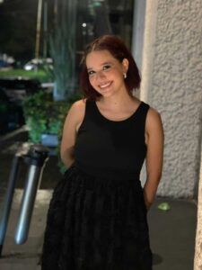 Fotografía en plano medio de Sofía. Ella es una mujer joven de piel blanca y cabello corto. Luce sonriente portando un vestido negro.
