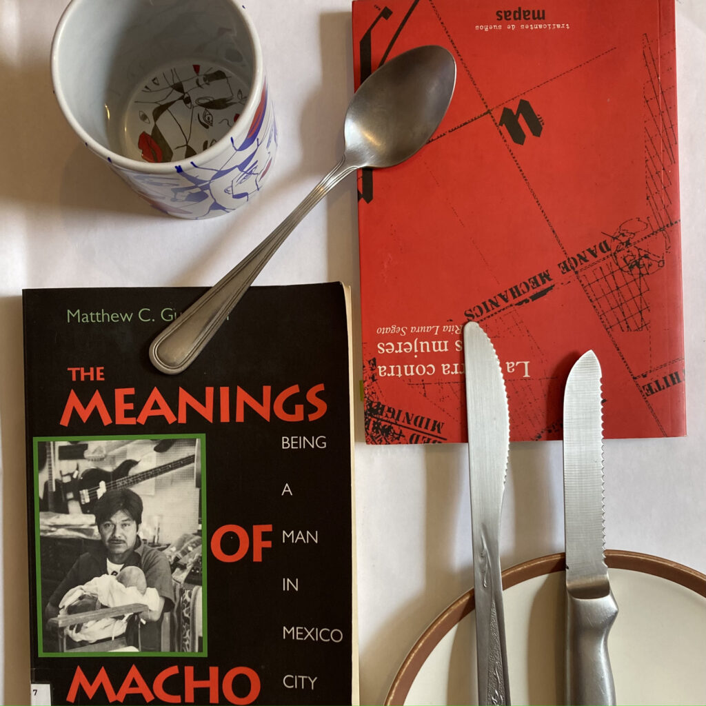 Fotografía donde se ven los libros “The Meanings of Macho: Being a Man in Mexico City” de Matthew C. Guttman y “La guerra contra las mujeres” de Rita Laura Segato, acompañadas de unos cubiertos.