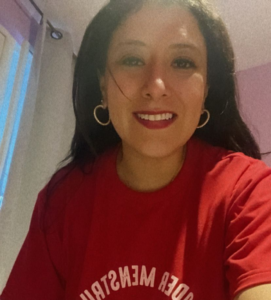 Fotografía de Anahí. Ella es una mujer joven que tiene el cabello largo y usa una playera color rojo que tiene el estampado de un puño en alto. 