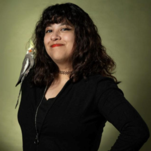 Fotografía de Jenny. Ella es una mujer joven que tiene el cabello ondulado a la altura del hombro. Le acompaña un ave con cabeza amarilla en su hombro derecho.