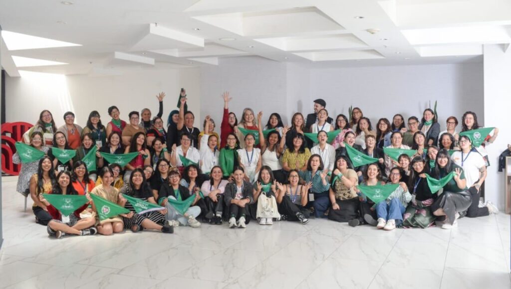 Fotografía en plano general donde se ve a varias mujeres. Algunas sostienen un pañuelo verde abortero, otras gritan y otras más alzan el brazo y puño derecho.