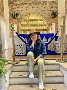 Fotografía de Verónica. Ella es una mujer de piel blanca que tiene el cabello castaño. Se le ve sentada en unas escaleras con la cara inclinada hacia la derecha y recargada sobre una de sus manos.