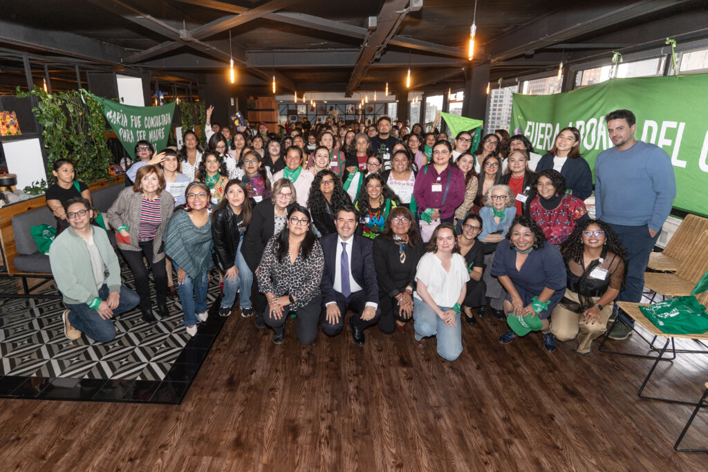 Fotografía de un grupo de personas. Algunas están en cuclillas mientras otras están paradas sosteniendo pañuelos verdes.